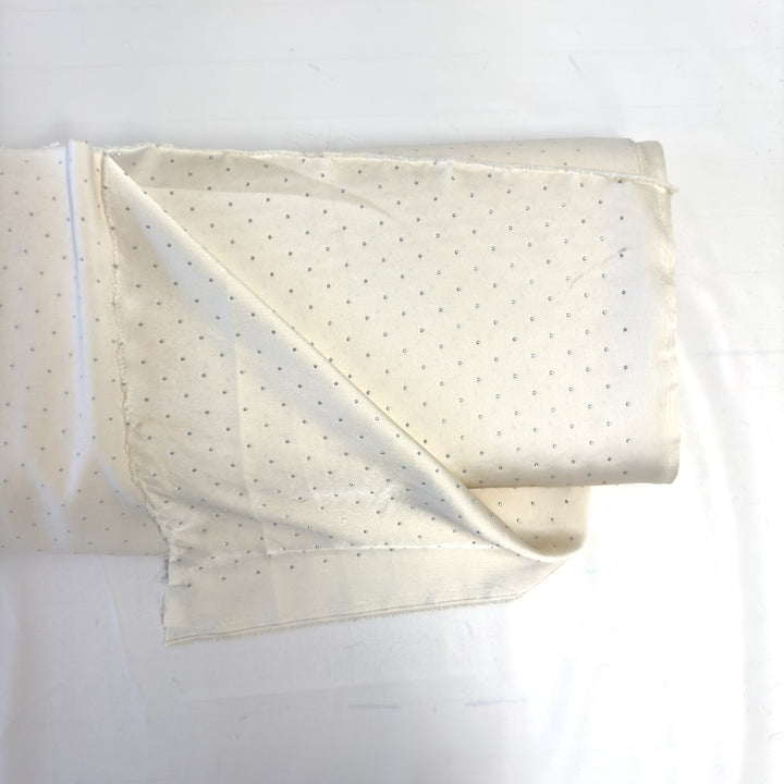 Bolt of cream rhinestone fabric with one end unfolded, on a white background