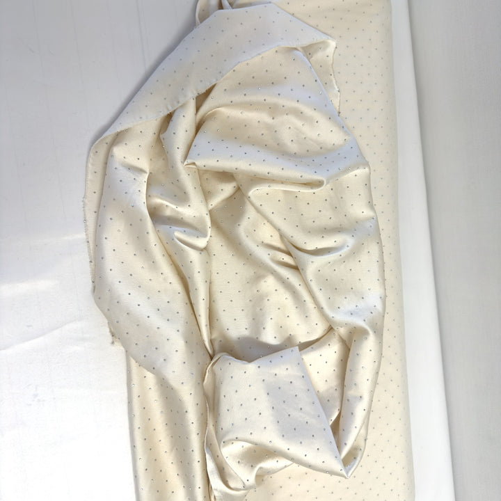 Cream rhinestone fabric unrolled over the bolt, seen from above