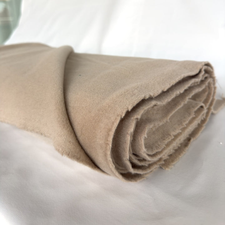 Roll of wool and cashmere coating fabric in sand, with its frayed selvedge