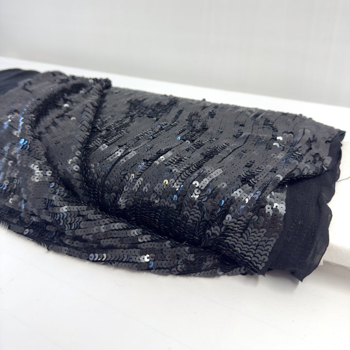 Tessuto con paillettes nere ripiegato sul rotolo, con il bordo in chiffon nero