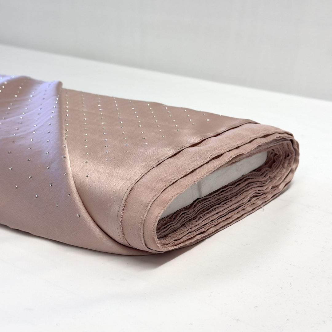 Roll of pink silk fabric with rhinestones on a white background