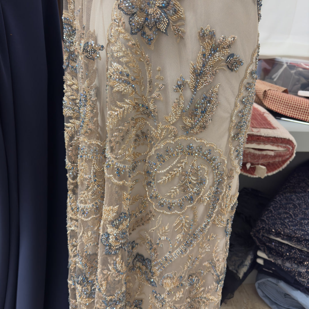 Tulle beige sabbia ricamato a fiori oro e blu, fotografato nel negozio Crilù a Trevi