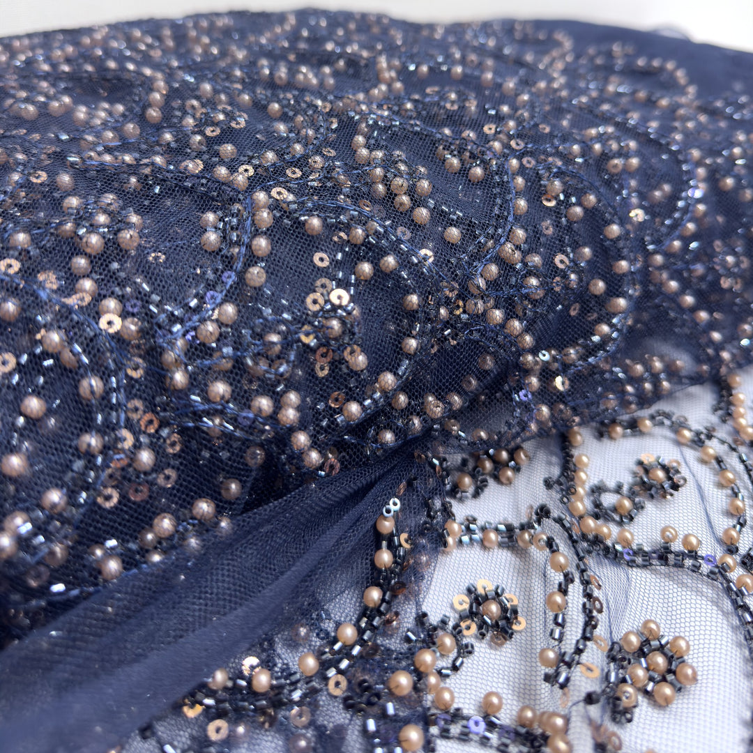 Gros plan sur la broderie : petites perles, perles couleur bronze et paillettes sur le tulle bleu